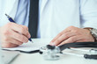 © cameravit - Mid section of male doctor writing write prescription to patient at worktable. Panacea and life save, prescribing treatment.