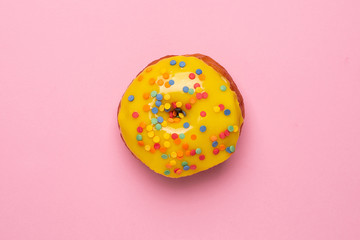 Sweet yellow donut with sprinkle on a pink background flat lay