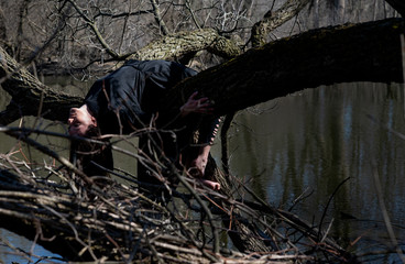 Woman with dark long hair in black robes hanging on tree branches in the middle of a swamp. Halloween and Gothic concept. Witchcraft and magic. Witch.