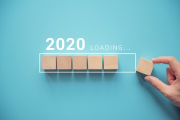 Loading new year 2020 with hand putting wood cube in progress bar.