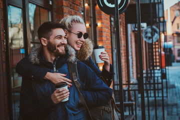 Cheerful smiling couple is enjoying their coffee outside cozy cafeteria, woman is hugging her man.