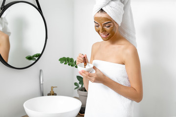 Beautiful young woman applying facial mask at home