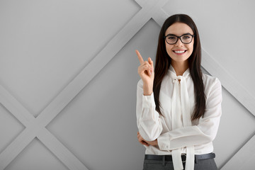 Beautiful young businesswoman with raised index finger on light background