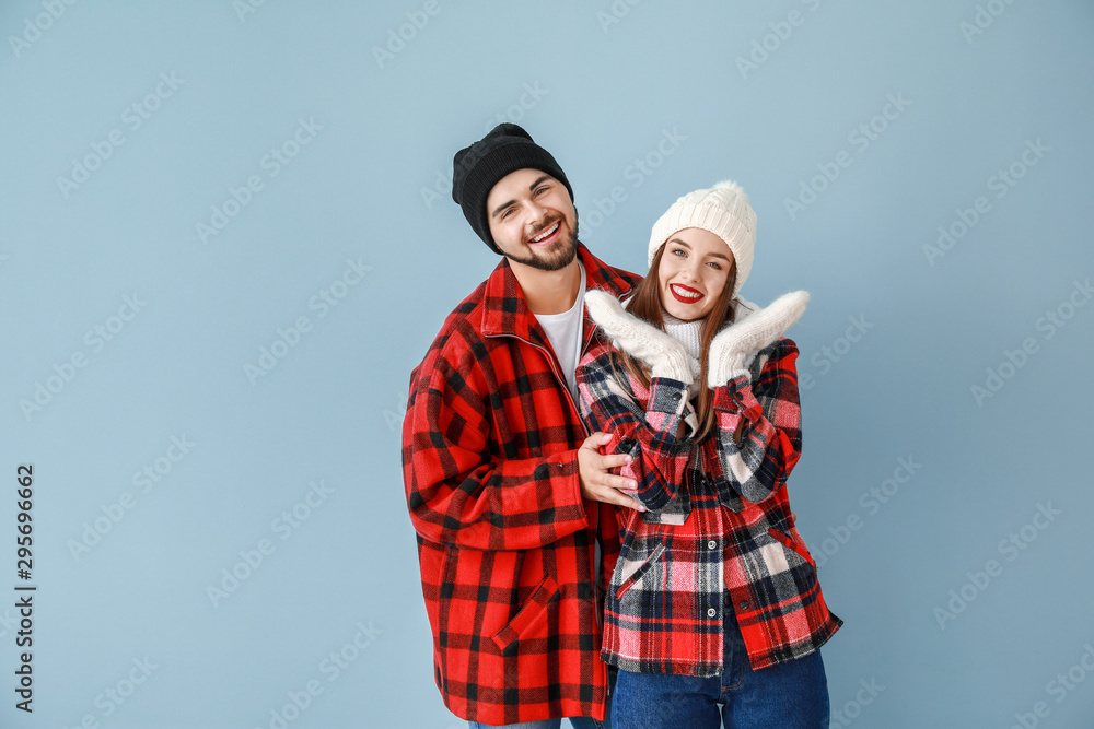 Happy young couple in warm winter clothes on color background