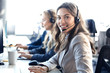 © ty - Female customer support operator with headset and smiling, with collegues at background.