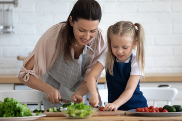 Caring mother teaching little daughter to cook salad