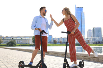 Lovely couple having fun driving electric scooter along the city promenade