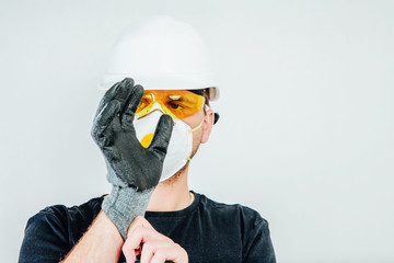 Poster - A worker wearing a protective helmet, protective goggles and a protective mask puts on protective gloves. Work concept, hiring workers for construction. Preparation to work.