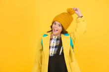 Warm And Stylish. Happy Small Schoolgirl Touch Stylish Pompom Hat. Little Child Smile With Stylish Autumn Look On Yellow Background. Stylish And Comfortable