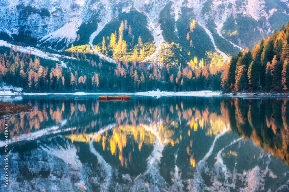 Braies lake with beautiful reflection in water at sunrise in autumn in Dolomites, Italy. Landscape with fall forest, mountains, lake, water, boats, trees with colorful foliage. Dolomiti. Italian alps - obrazy, fototapety, plakaty 