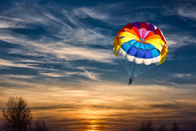 People Are Gliding With A Parachute On The Background Of Sunset.