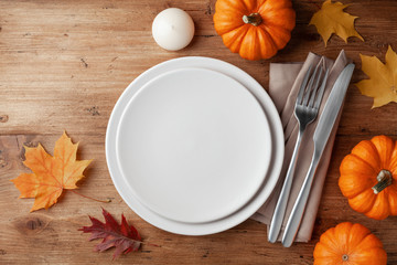 Autumn Thanksgiving table setting for dinner with plate, knife, fork decorated pumpkins and maple leaves. Top view.