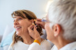 © Dragana Gordic - Mature female doctor hearing specialist in her office trying hearing aid equipment to a patient elderly senior woman. Senior woman adjusting hearing aid in doctor's office