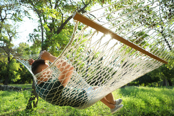 Wall Mural - Young man resting in comfortable hammock at green garden