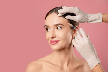 Wall Mural - Beautiful woman getting facial injection on pink background. Cosmetic surgery