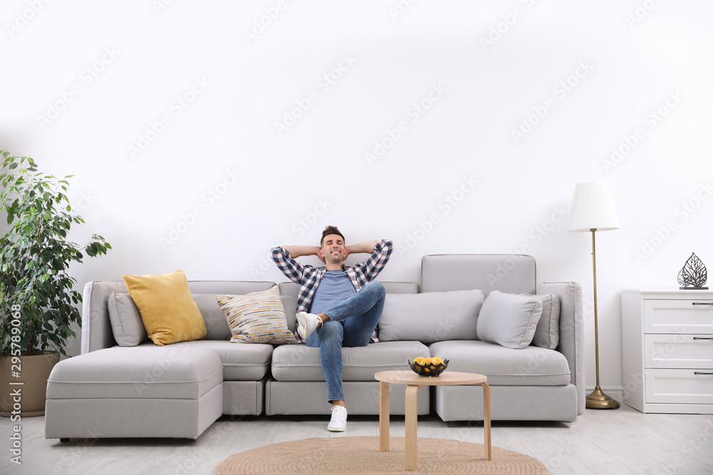 Young man relaxing on sofa under air conditioner at home - obrazy, fototapety, plakaty 