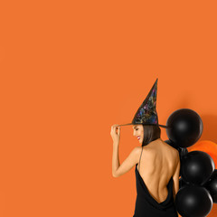 Wall Mural - Beautiful woman wearing witch costume with balloons for Halloween party on yellow background, space for text