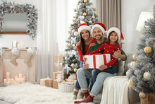 Portrait Of Happy Family With Christmas Gift At Home, Space For Text