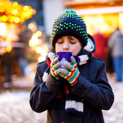 Wall Mural - Little cute kid boy drinking hot children punch or chocolate on German Christmas market. Happy child on traditional family market in Germany, Laughing boy in colorful winter clothes