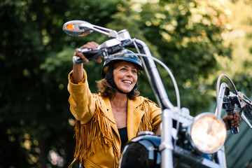 Cheerful senior woman traveller with motorbike in town.