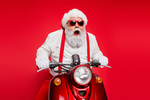 Portrait Of Nice Attractive Bearded Crazy Cheerful Cheery Funny Funky Santa Riding Motor Bike Delivering Shop Orders Hurry Up Isolated Over Bright Vivid Shine Vibrant Red Color Background