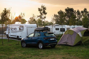 Caravans and campers on green meadow in campsite. Sunrise, rays on campers in the morning.