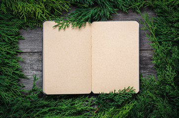 Wall Mural - Christmas frame from fir branches on a background of an old gray board around an open notebook with blank sheets. Frame of fir branches. Christmas card blank concept.