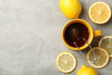 Cup of tea and lemons on grey background, space for text