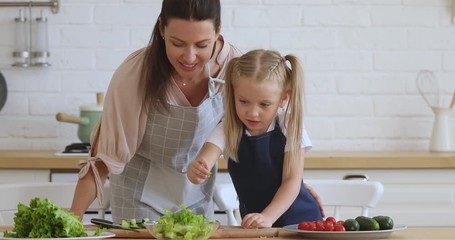 Wall Mural - Kid daughter learning cooking helping mom cut vegetable salad