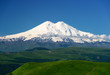 Great nature mountain landscapes. Fantastic perspective of caucasian snow inactive volcano Elbrus with green fields and road to it and clearly blue sky background. Russia