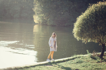 Wall Mural - a young beautiful woman in a coat and pants walking in the park by the water