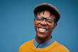 © Seventyfour - Head and shoulders portrait of excited African-American man smiling happily while posing against blue background wearing bright knit sweater