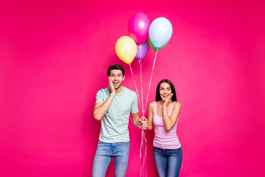 Photo of funny guy and lady holding air balloons arms on cheeks not believe unexpected surprise from friends wear casual outfit isolated pink color background