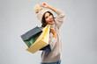 © Syda Productions - christmas, seasonal sale and consumerism concept - happy smiling young woman in knitted winter hat and sweater with shopping bags over grey background