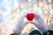 Woman hands in white knitted mittens with a red heart on a snow background.