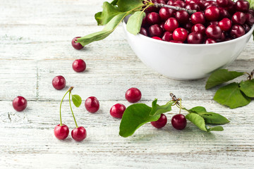 Fresh sweet cherries white bowl with leaves in water drops on wooden background