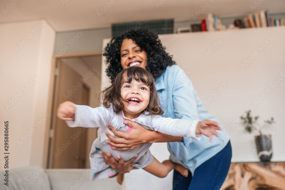 Mother playfully swinging her little daughter in the air - obrazy, fototapety, plakaty 