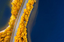 Aerial View Of Road Between Yellow Orange Autumn Forest And Blue Lake In Finland
