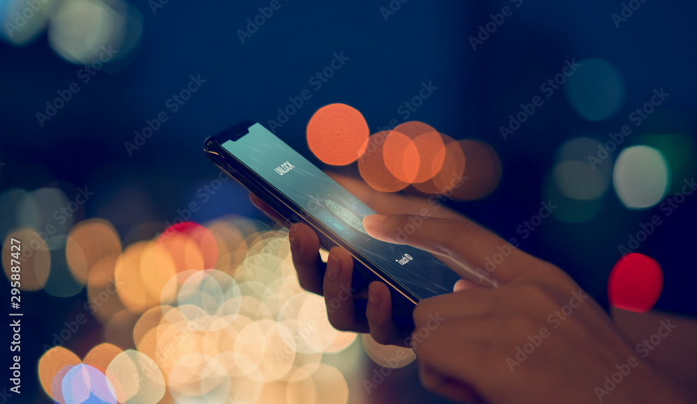 Close-up of hands scanning fingerprint on smartphone to unlock mobile phone on bokeh colors light in night atmospheric city, Concept security in identity technology. - obrazy, fototapety, plakaty 