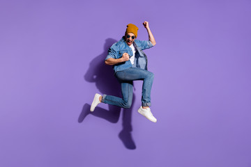 Poster - Full length body size photo of cheerful ecstatic screaming guy wearing jeans denim jacket overjoyed with victorious glory jumping up brown cap isolated over purple vivid color background