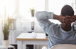 © Prostock-studio - Black worker sitting in office with hands behind his head