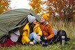 trekking and hiking concept - portrait of cute couple sitting near green tent in autumn forest