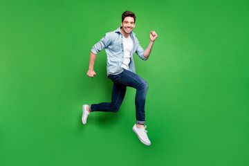 Full body profile photo of handsome guy jumping high sportive competition participant running fast wear casual denim clothes isolated green color background