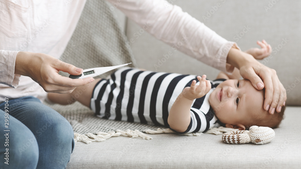 Mother holding thermometer measuring temperature of her sick baby