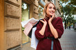© Anton - Portrait of attractive smiling blond girl with shopping bags happily looking away on street