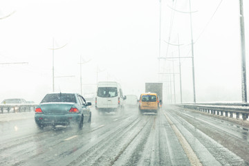 Cars drive along road with slush, snowstorm. City traffic in snow blizzard.