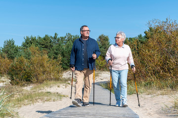 Happy elderly couple walking in a dunes. Active senior lifestyle concept. Nordic walking