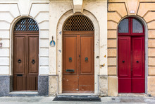 Three Old Wooden Arched Doors, Brown And Red, Decorated With Iron Door Knockers And Molding. Vintage Entry Doors In Valletta, Malta.