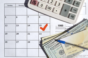 1065 Return of partnership income blank with dollar bills, calculator and pen on calendar page with marked 15th April