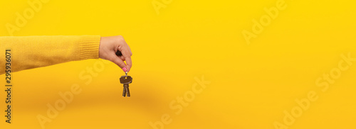 Fotografía female hand holding house keys, suggesting, over yellow background, panoramic image